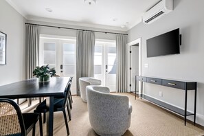 A modern room with a dark wooden table, two grey armchairs, a black console table, and a mounted TV. - Thomas Waring House | Unit D | Sleeps 6 (Charleston)