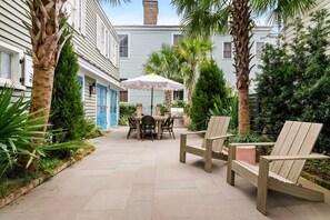 A patio area with a table and chairs, surrounded by plants and a palm tree. - Thomas Waring House | Unit D | Sleeps 6 (Charleston)