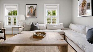 A modern living room with a sectional sofa, a coffee table with a tray, and two windows with shutters. - Thomas Waring House | Unit D | Sleeps 6 (Charleston)