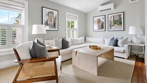 A modern living room with a white sofa, a wooden coffee table, and a wicker chair. - Thomas Waring House | Unit D | Sleeps 6 (Charleston)