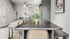 A modern dining area with a long table, chairs, and a potted plant. - Thomas Waring House | Unit D | Sleeps 6 (Charleston)