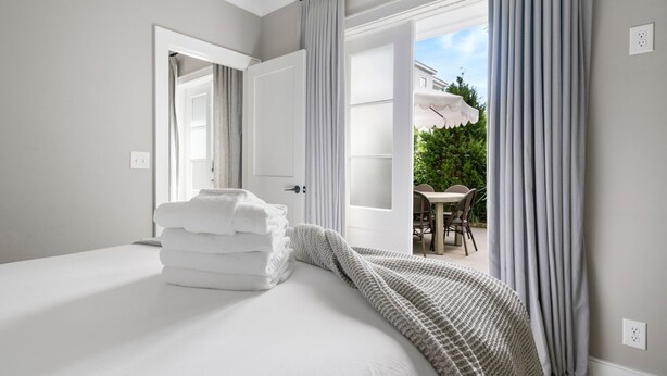 A hotel room with a bed, a stack of towels, and a view of an outdoor patio with a table and chairs.