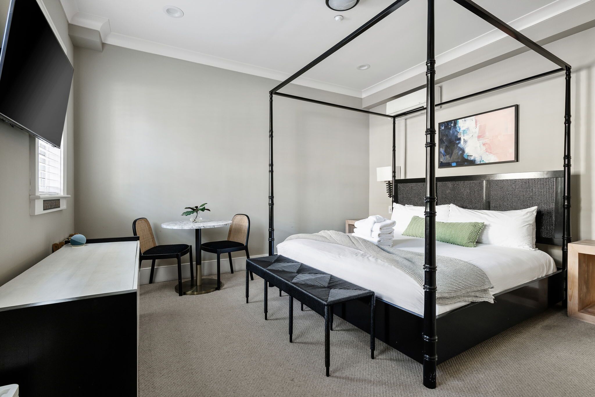 Een hemelbed met hoofdbord, een bureau met stoel, een kleine ronde tafel met stoel en een potplant.