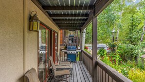 A covered patio with outdoor seating, a grill, and a view of a garden. - All Seasons | B1 - 3 Bedroom/ 2 bath condo Vail Village (Vail)