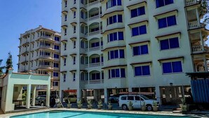 A multi-story hotel with balconies, a swimming pool, and parked vehicles. - Clalem Bay Condos by RevSerene (Mombasa)
