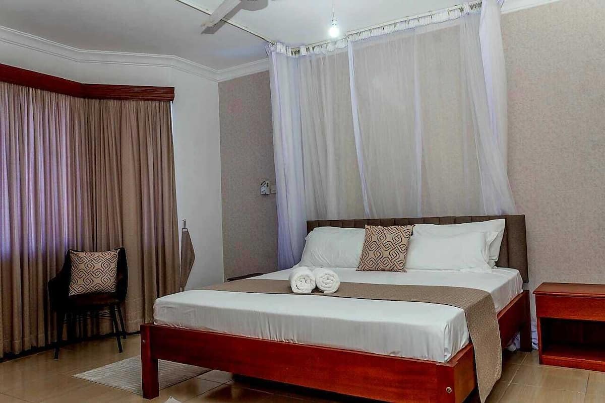 A hotel room with a large bed, a chair, a bedside table, and a curtain.