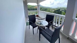 Un balcon avec une table et des chaises, un pot de fleurs et une vue sur la verdure.