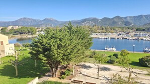 A marina with boats docked, a large tree in the foreground, and mountains in the background. - Sublime new apartment on the beach in ST FLORENT, 5' from the center (Saint-Florent)
