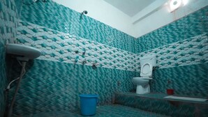 A bathroom with a patterned tile wall, a toilet, a blue bucket, and a sink.
