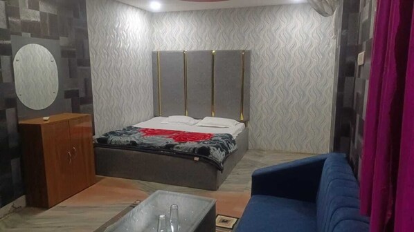 A bedroom with a bed, a wooden cabinet, a blue sofa, and a small table with a bottle. - Hotel Parinay Vatika Deoghar (Deoghar)