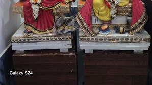 Two statues of deities on pedestals, with a framed picture and a small shrine in the background.