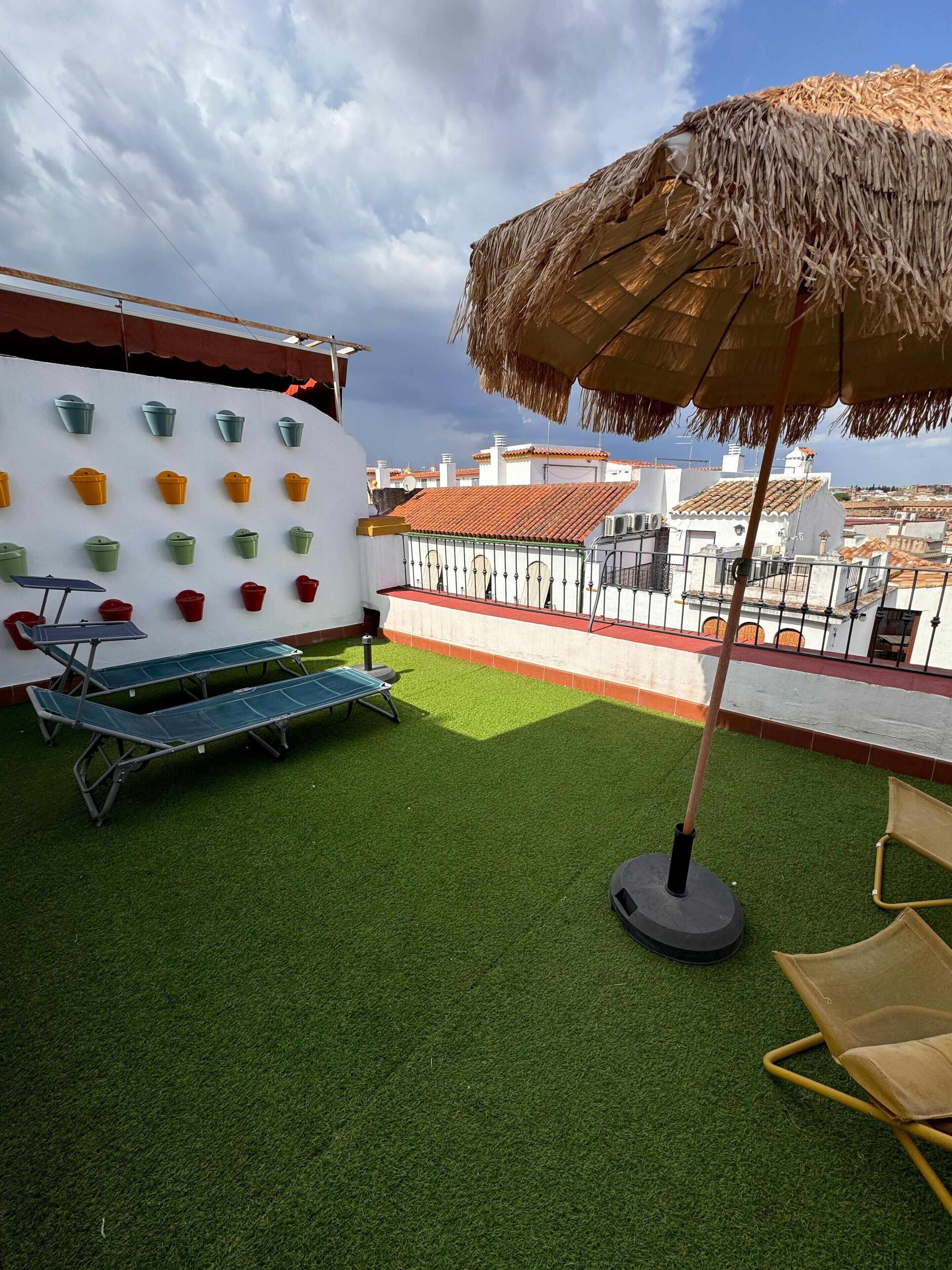 Een dakterras met kunstgras, een zithoek, een muur met kleurrijke emmers en een rieten parasol.