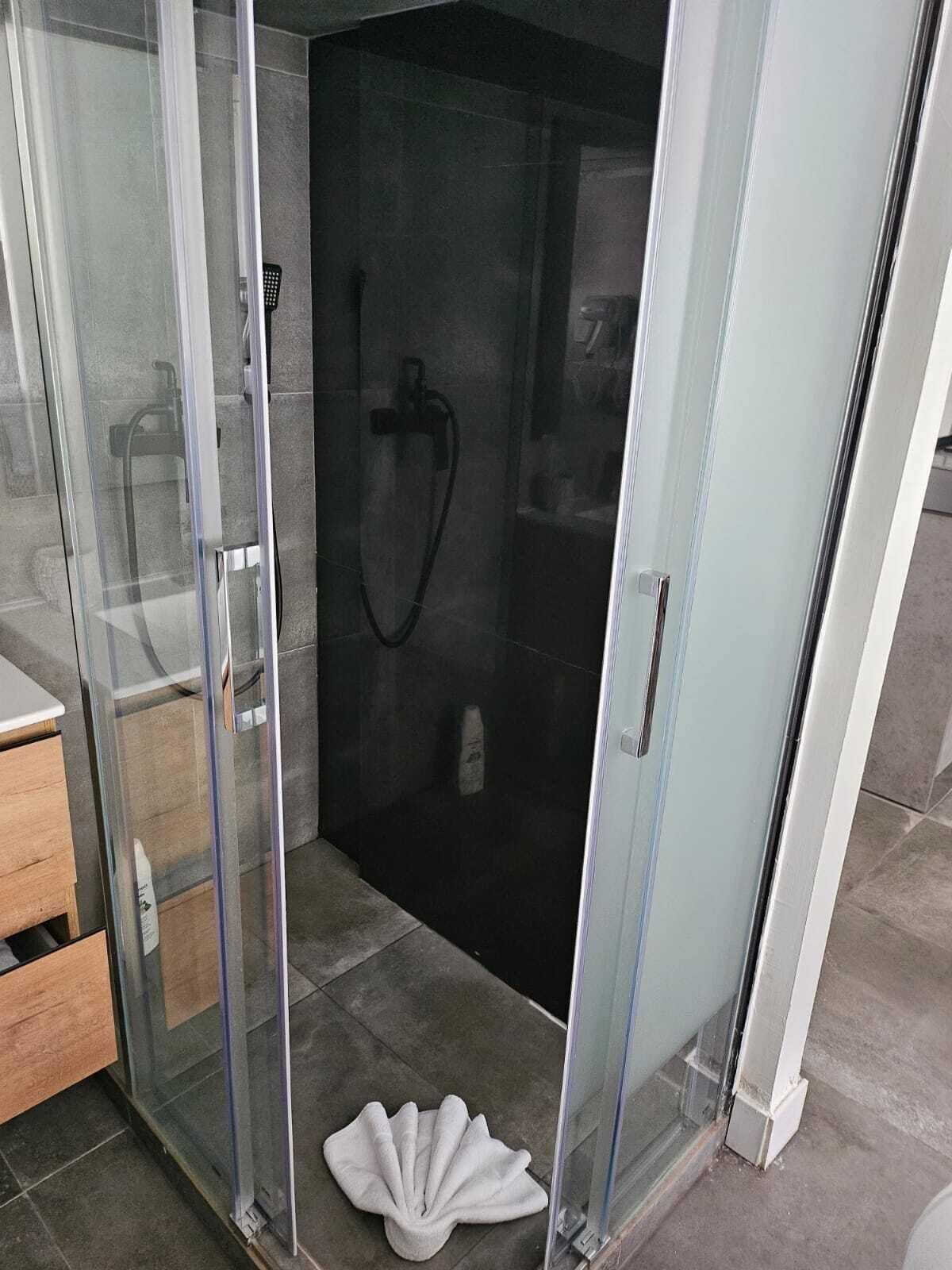 Un baño moderno con ducha de vidrio, tocador de madera y una toalla blanca en el suelo.