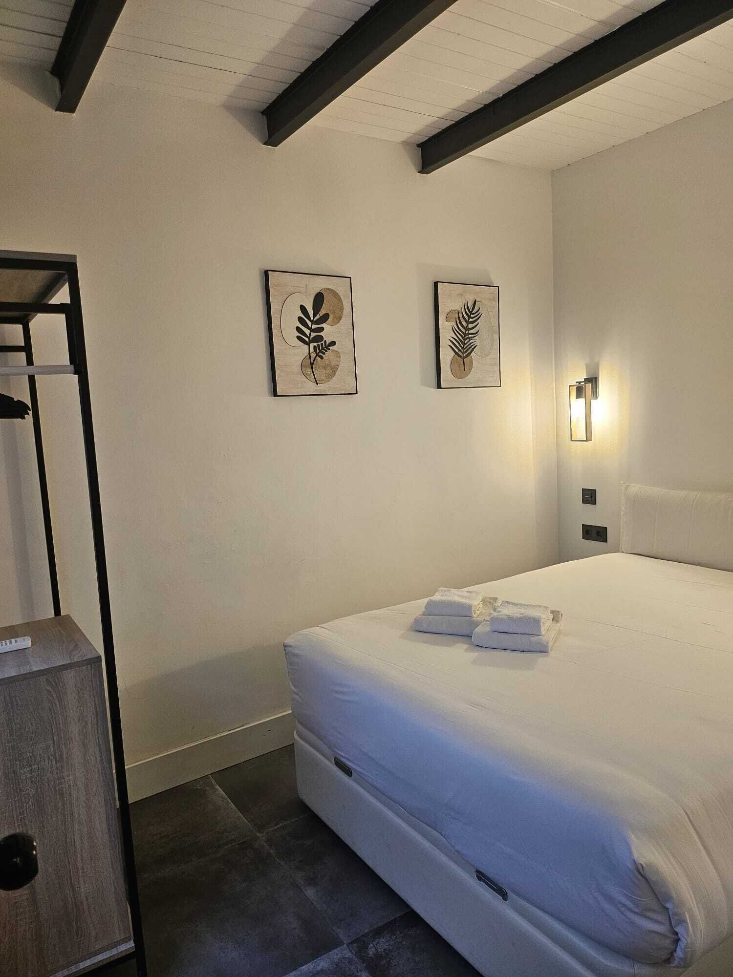 A modern bedroom with a large bed, a wooden nightstand, and two wall-mounted artworks.