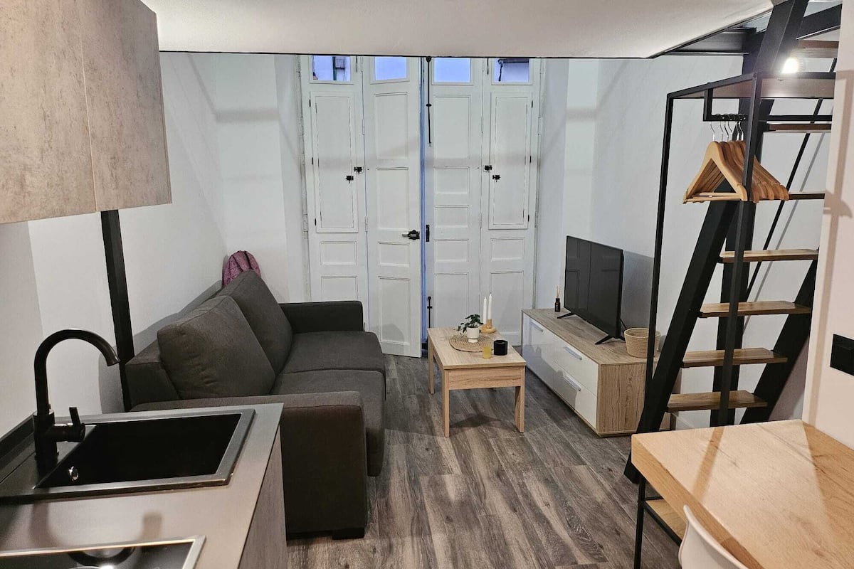 A compact living space with a kitchenette, a sofa, a TV, and a wooden table.