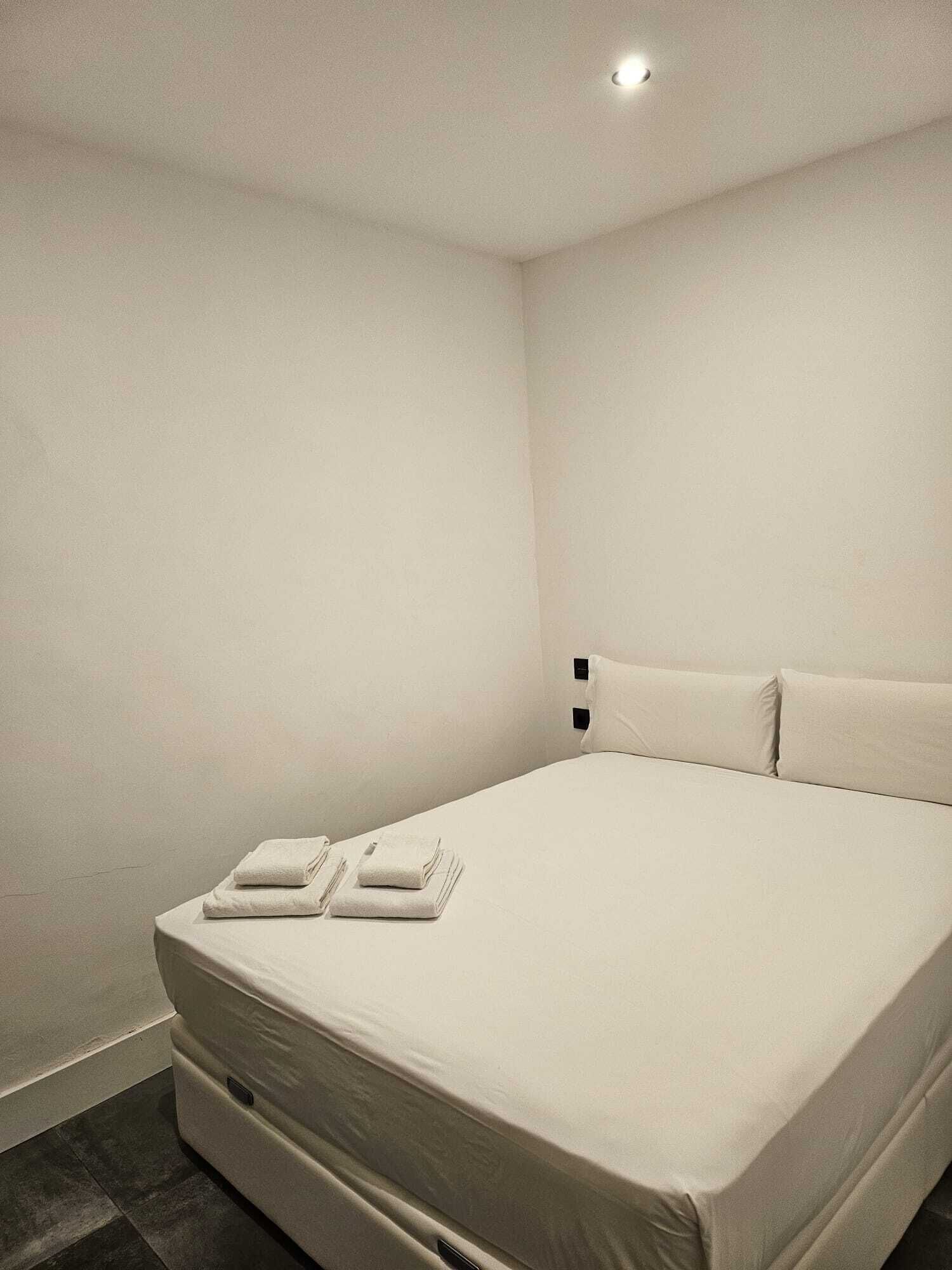 Habitació d'hotel minimalista amb un llit individual, dos almoines i dues tovelloles doblegades.