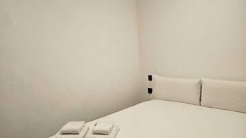 Habitació d'hotel minimalista amb un llit individual, dos almoines i dues tovelloles doblegades.