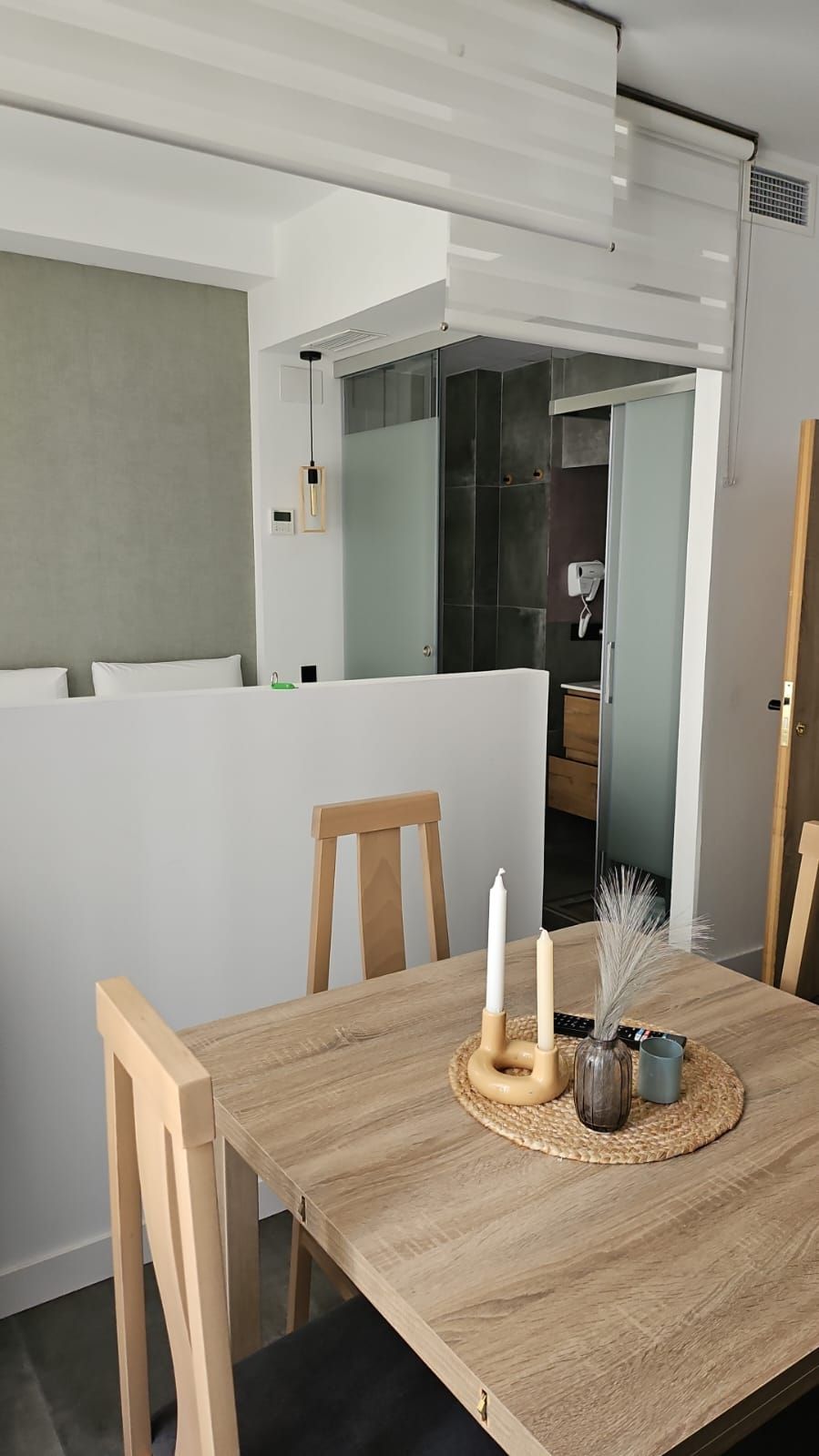 Un comedor moderno con una mesa de madera, dos sillas y un florero con velas.
