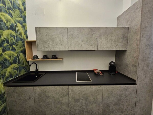 A modern kitchen with grey cabinets, a black countertop, and a small wooden shelf.