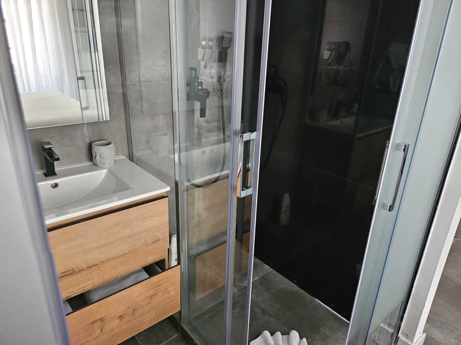 A modern bathroom with a glass shower enclosure, a wooden vanity, and a white sink.
