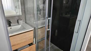 A modern bathroom with a glass shower enclosure, a wooden vanity, and a white sink.
