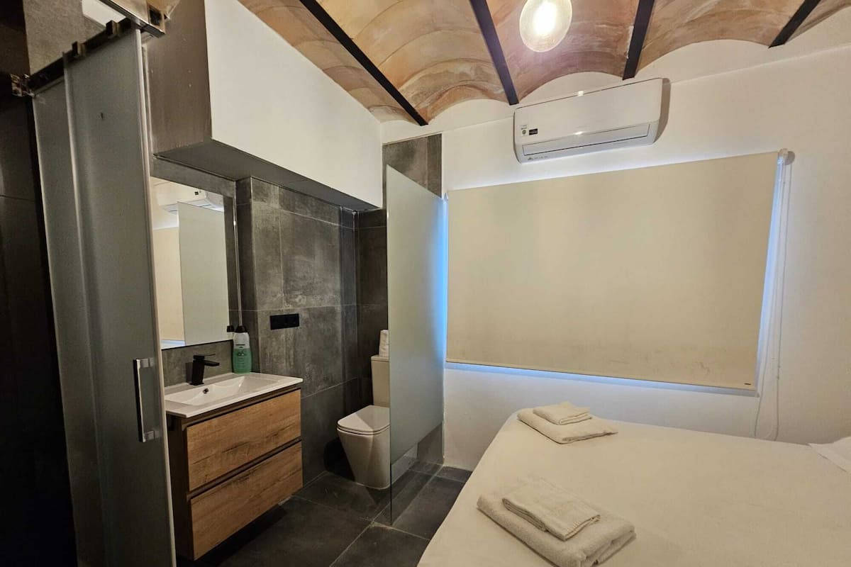 A modern bathroom with a wooden vanity, a mirror, a toilet, and a bed with towels.