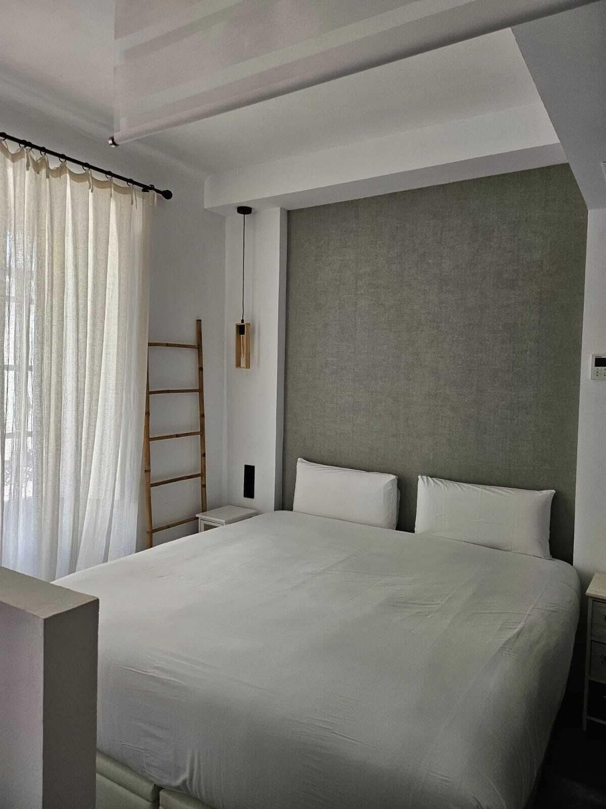 Un dormitorio moderno con una cama grande, una escalera de madera, una mesita de noche y un aplique de pared.