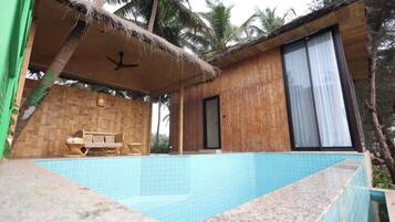A poolside area with a wooden deck, a thatched roof, and a wicker sofa.