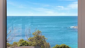 Blick auf das Meer durch ein Fenster, mit blauem Himmel und etwas Vegetation im Vordergrund.
