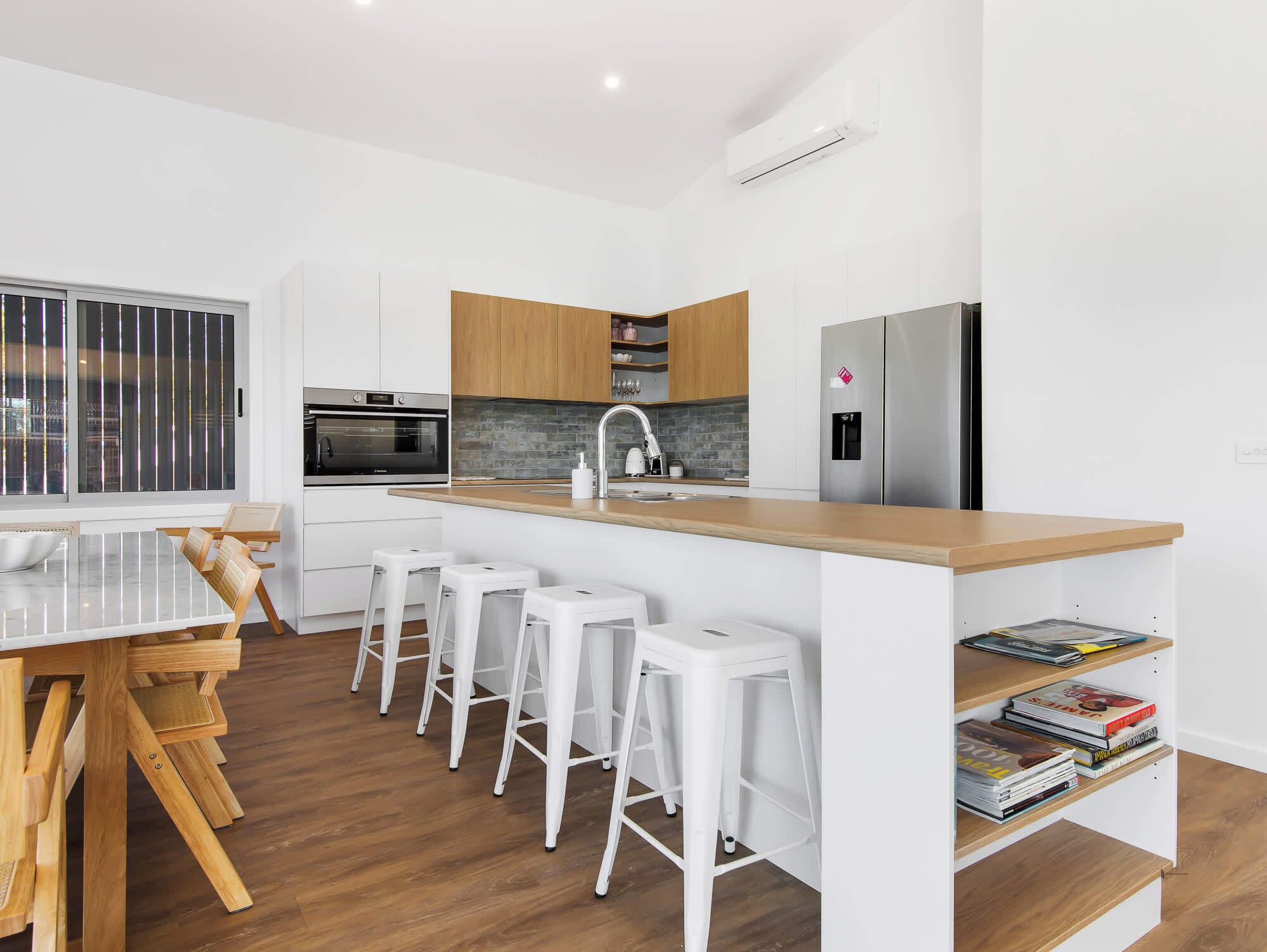 Una cocina moderna con una isla central, taburetes de bar, horno empotrado y un refrigerador de acero inoxidable.