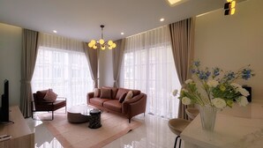 A modern living room with a leather sofa, a coffee table, and a vase of flowers. - Villa NovaWorld Phan Thiet 9 Trip STay (Tien Thanh)