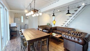 A modern kitchen with a wooden dining table, leather sofa, and hanging pendant lights. - Vamos Villa Tokunoshima (Tokunoshima)