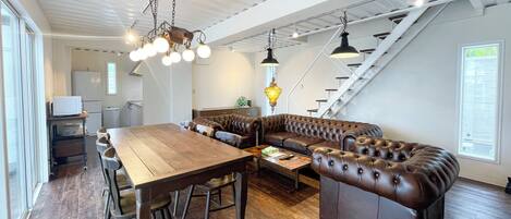 A modern kitchen with a wooden dining table, leather sofa, and hanging pendant lights.