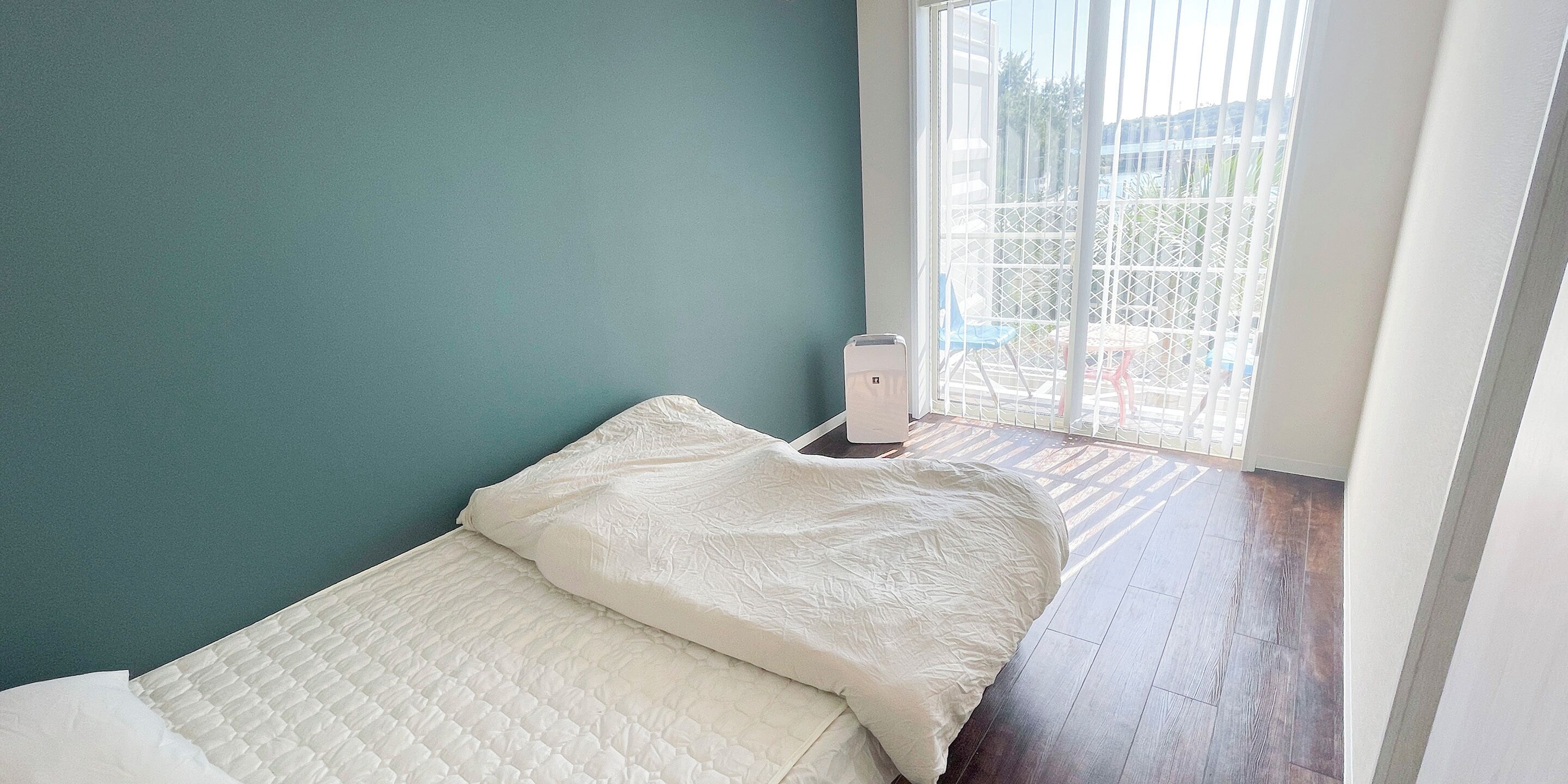 A small, neatly made bed with a white quilt in a room with teal walls and a wooden floor.