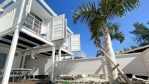 A white building with a balcony, a palm tree, and a table with chairs. - Vamos Villa Tokunoshima (Tokunoshima)