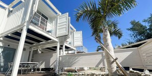 A white building with a balcony, a palm tree, and a table with chairs. - Vamos Villa Tokunoshima (Tokunoshima)