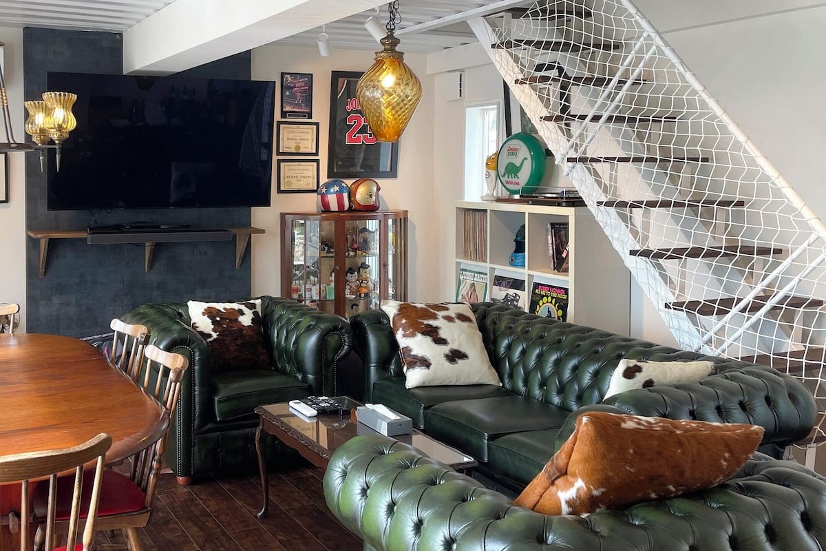 Ein modernes Wohnzimmer mit einem großen Flachbildfernseher, einem Holzesstisch, grünen Ledersofas und einer weißen Wendeltreppe.