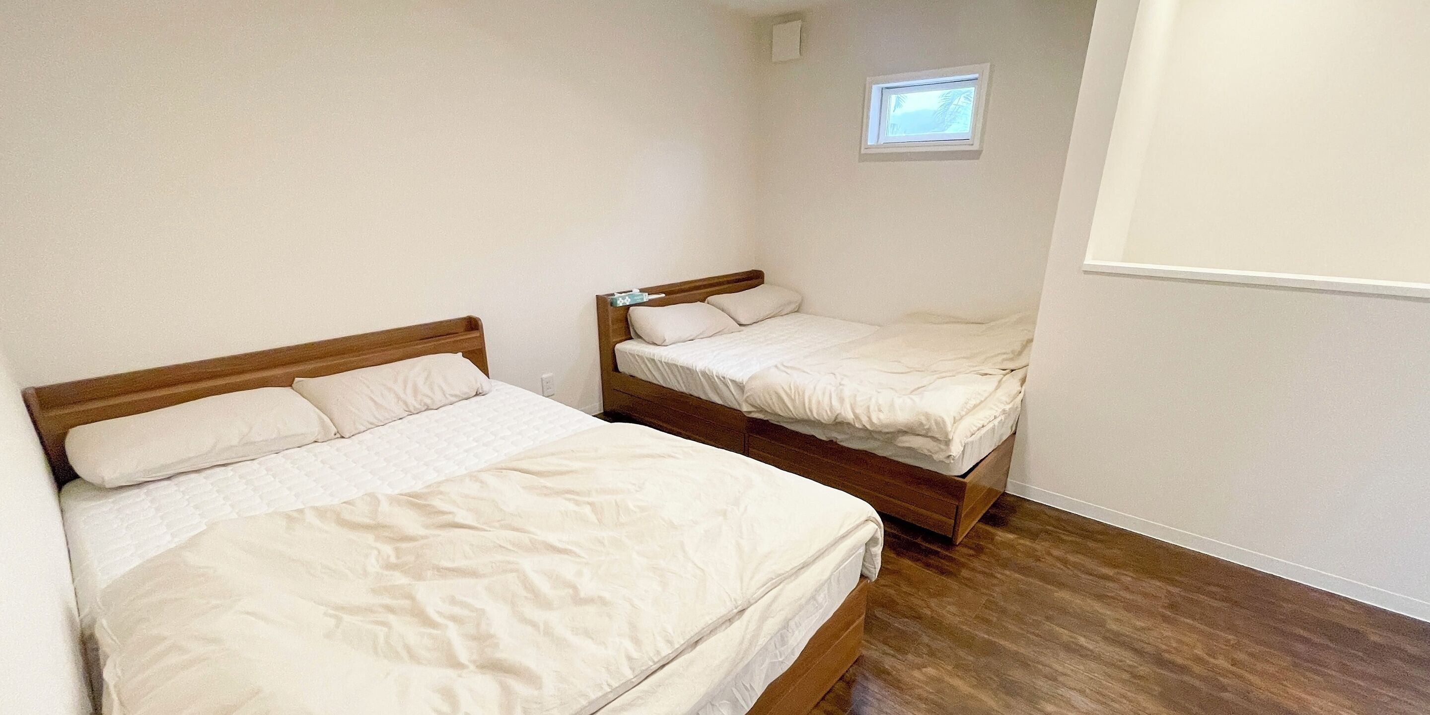 A bedroom with two single beds, wooden headboards, and a small window.