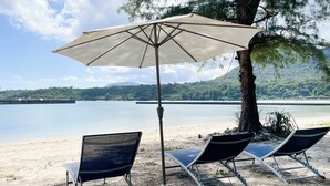 A beach with a large umbrella, two lounge chairs, and a view of a lake and mountains. - Vamos Villa Tokunoshima (Tokunoshima)