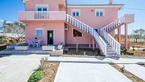 A two-story pink house with a staircase leading to the upper floor, a small patio with outdoor furniture, and a clear sky. - Apartments Perinic (Vrsi)