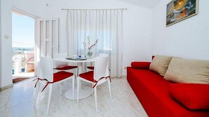A modern living room with a red sofa, white dining table with red chairs, and a view of the sea through large windows. - Apartments Perinic (Vrsi)