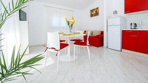 A modern kitchen with red cabinets, a white refrigerator, and a dining area with a white table and chairs. - Apartments Perinic (Vrsi)