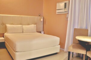 Habitación de hotel con una cama grande, una mesita de noche, una silla y un equipo de aire acondicionado en la pared.