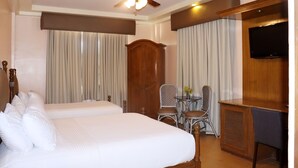 Een hotelkamer met een bed, een bureau, een stoel, een televisie en een plafondventilator.