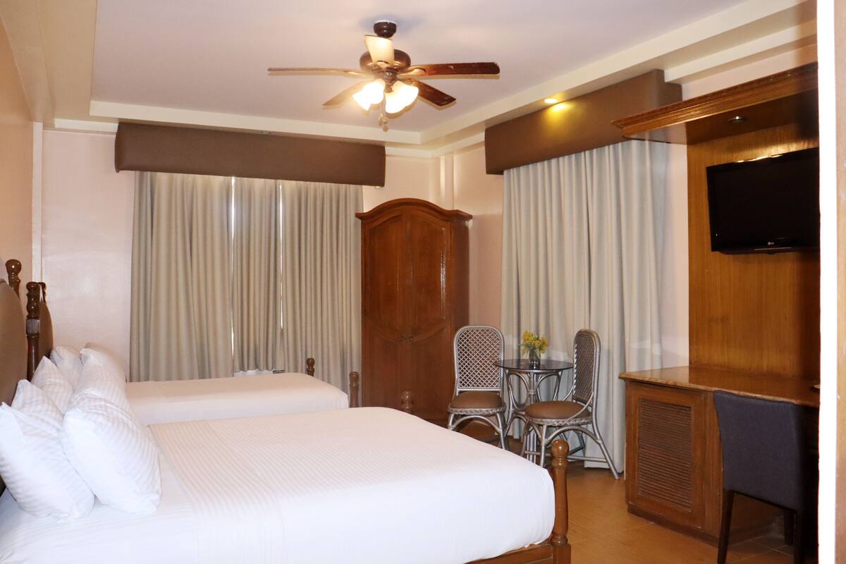 A hotel room with a bed, a desk, a chair, a television, and a ceiling fan.