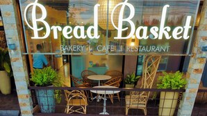 De gevel van Bread Basket Bakery Cafe Restaurant met rieten meubels en potplanten.