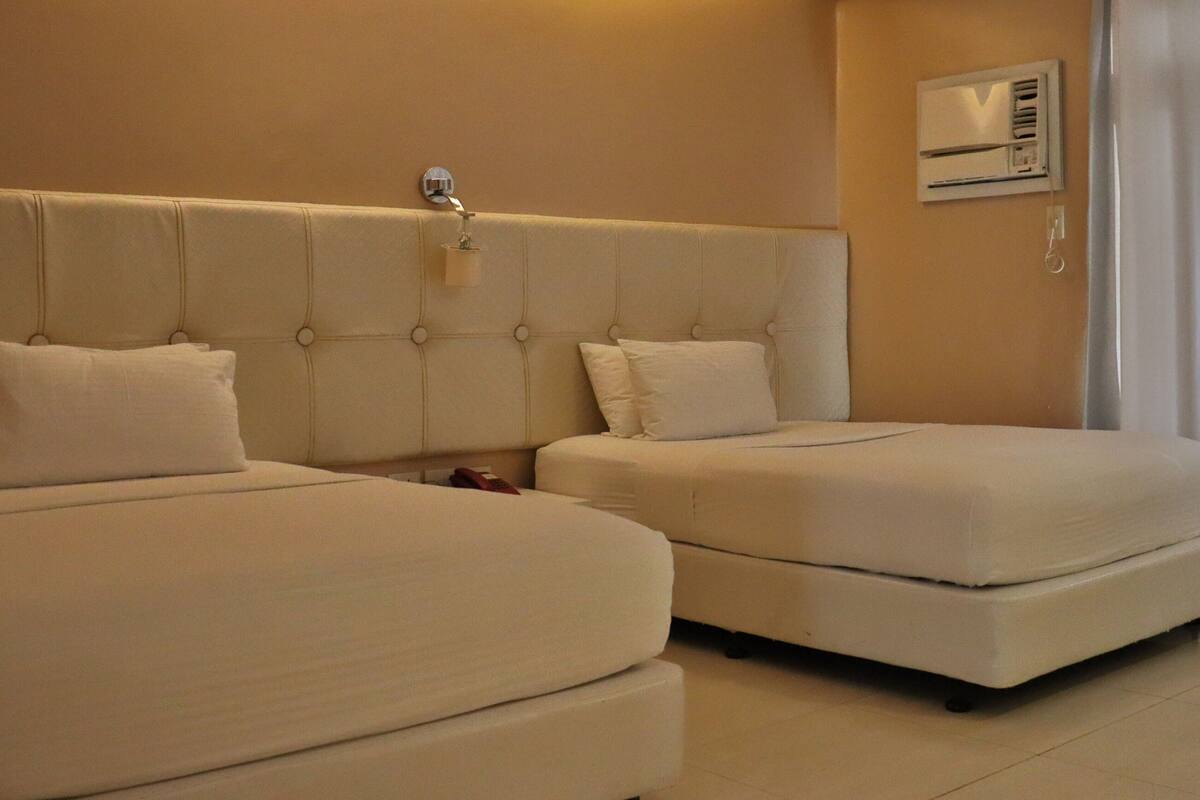 A hotel room with two beds, a wall-mounted air conditioning unit, and a curtain on the window.