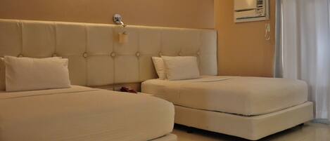 A hotel room with two beds, a wall-mounted air conditioning unit, and a curtain on the window.