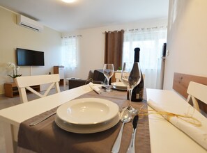A dining area with a table set for two, a bottle of wine, and a television in the background. - Stylish and Modern Rovinj Apartment (Rovinj)