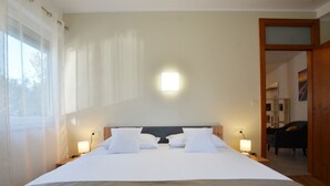 A neatly made bed with white linens and pillows, a bedside table with a lamp, and a window with sheer curtains. - Stylish and Modern Rovinj Apartment (Rovinj)